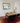 A rustic wooden dining table with a black metal frame and six black chairs, set on a red patterned area rug in a dining room with white wainscoting and a large gold-framed mirror.